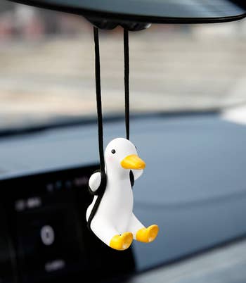 A white duck figure suspended on a black swing from a car mirror