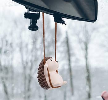 A hedgehog suspended on a black swing from a car mirror
