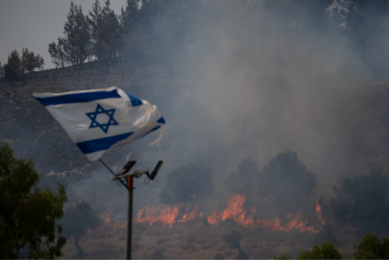 Bendera Israel berkibar di samping api yang berkobar di kawasan dekat perbatasan dengan Lebanon, Israel utara di Safed, Rabu, 12 Juni 2024.