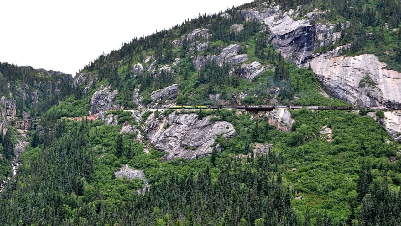 <p>Starting in the port town of Skagway, Alaska, and climbing up to the White Pass summit at 2,888 feet, <a href="https://www.wpyr.com/" rel="noopener">train passengers</a> are treated to stunning views of towering mountains, cascading waterfalls, deep gorges, and dense forests.</p><p>The route includes cliff-hanging turns, tunnels, and trestle bridges, including the 215-foot-tall steel cantilever bridge. You’ll follow the Klondike Gold Rush route, where you can witness some historic landmarks.</p>