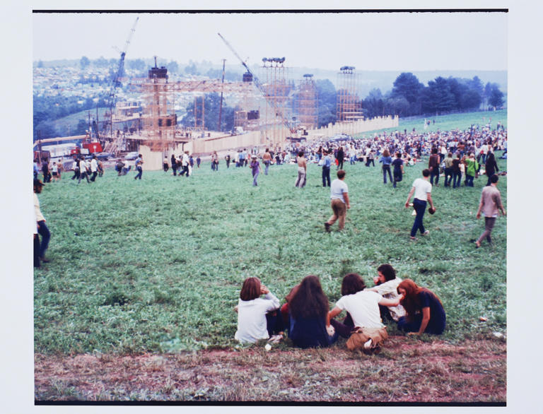 En esta fotografái de agosto de 1969 asistentes a la Feria de Música y Arte de Woodstock caminan en el terreno cerca del escenario principal. En Bethel, Nueva York la organización sin fines de lucro el Centro para las Artes Bethel Woods, que administra el sitio, tiene ahora nuevas instalaciones de campamento de lujo. (David Shelburne vía AP)