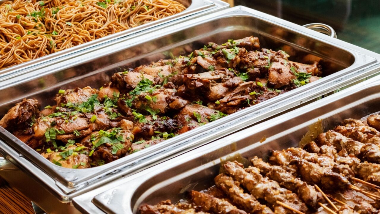 <p>You should avoid standing too close to the food trays while deciding what to take from the buffet.  This can make others uncomfortable and increases the risk of hair or other contaminants falling into the food. </p>