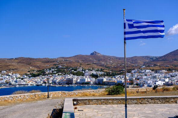Greek flag waving over blue sky with Tinos city