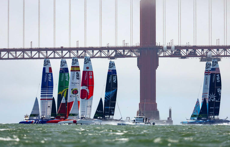 A fleet of F50 racing boats passes the Golden Gate Bridge during San Francisco SailGP racing tournament in 2023.