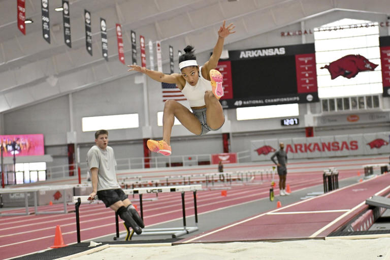 FILE - Olympic long jumper Tara Davis-Woodhall makes a practice jump at the Randal Tyson Track Center, Thursday Jan. 18, 2024, in Fayetteville, Ark., as Paralympic sprinter Hunter Woodhall looks on, at left. (AP Photo/Michael Woods, File)