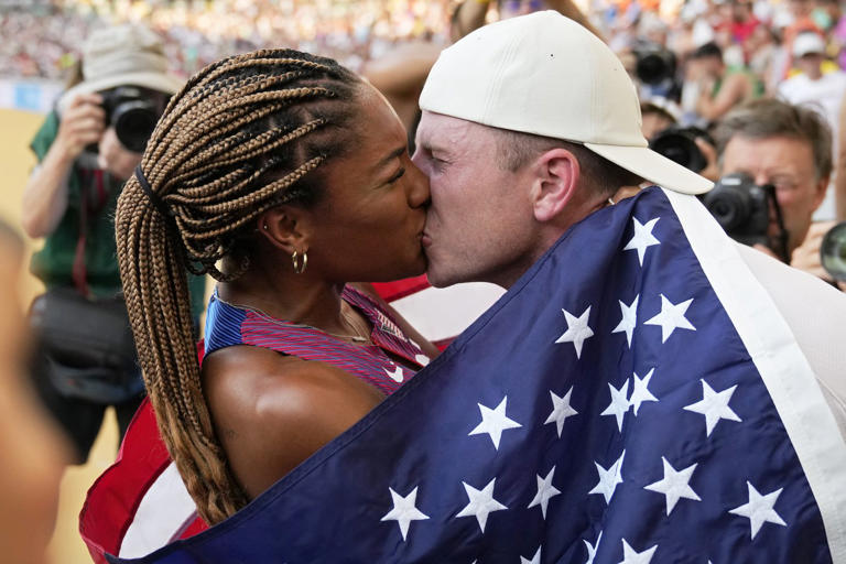 FILE - Tara Davis-Woodhall, of the United States, gets a kiss from her husband Hunter Woodhall after winning the silver medal in the women's long jump final during the World Athletics Championships in Budapest, Hungary, Sunday, Aug. 20, 2023. They are track and field's power couple. Long jumper Tara Davis-Woodhall and her husband, Hunter Woodhall, are on a quest to make this Olympic year better than any before it.(AP Photo/Matthias Schrader, File)