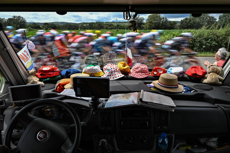 July 4: Stage 6 – The pack of riders (peloton) cycles past a parked car with Tour de France promotional hats lining the dashboard, during the 163.5-kilometer stage between Macon and Dijon, France.