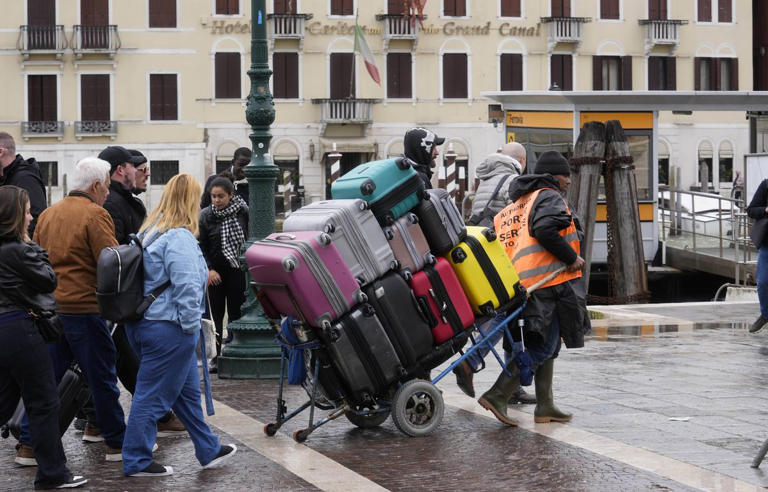Un homme transporte les bagages de touristes devant la gare principale de Venise, en Italie, le mercredi 24 avril 2024. (PHOTO D'ILLUSTRATION)
