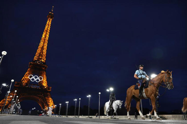 Mounted police officers ride near the Eiffel Tower on Tuesday night. The Paris Olympics opening ceremony will feature a flotilla of boats on the Seine and thousands of spectators, creating many security challenges. ((Wally Skalij / Los Angeles Times))