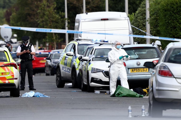 Des officiers de police et du personnel médico-légal se tiennent derrière un cordon sur Hart Street à Southport, dans le nord-ouest de l'Angleterre, le 29 juillet 2024, à la suite d'une attaque au couteau.