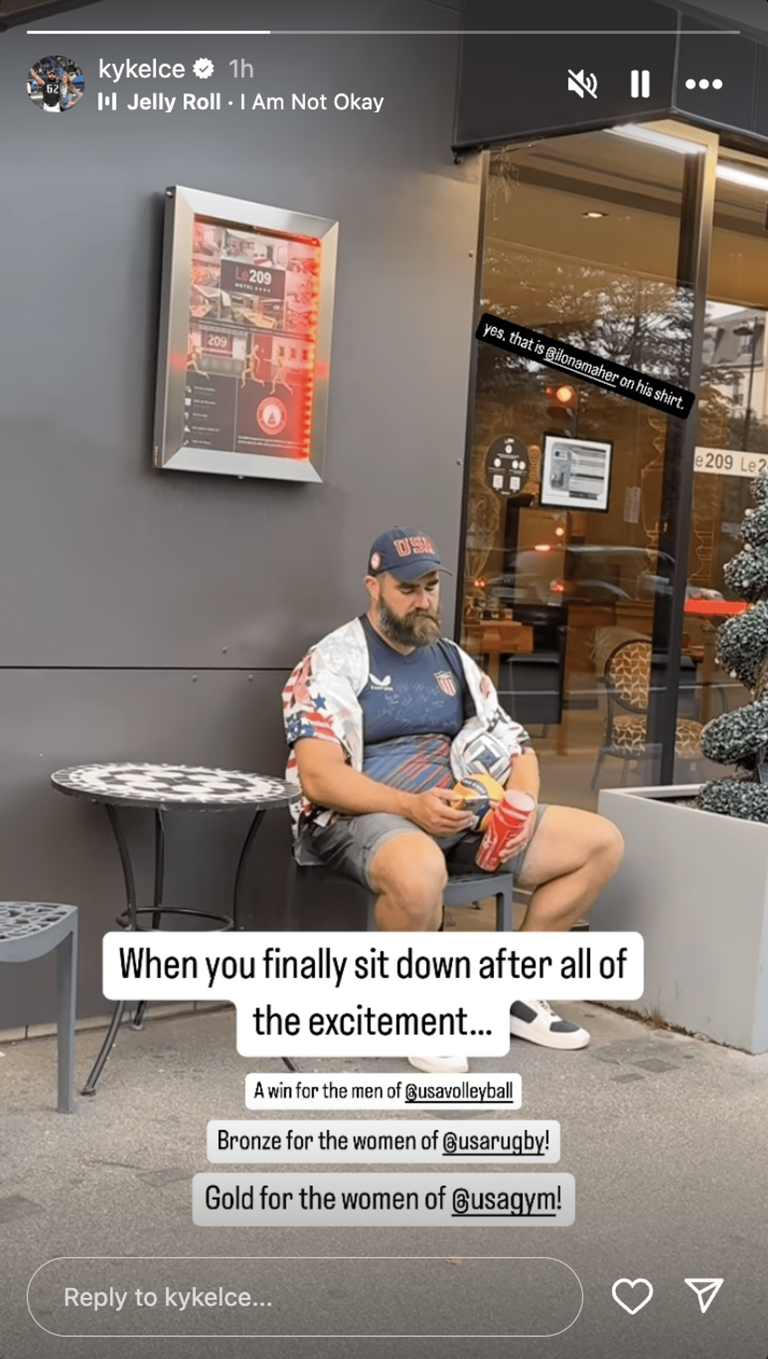 Jason Kelce in American-colored apparel sits outside a cafe and tiredly scrolls on his phone. (@KyKelce / Instagram)