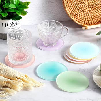 A collection of stylish glass coasters in pastel hues are displayed with elegant glass cups on top