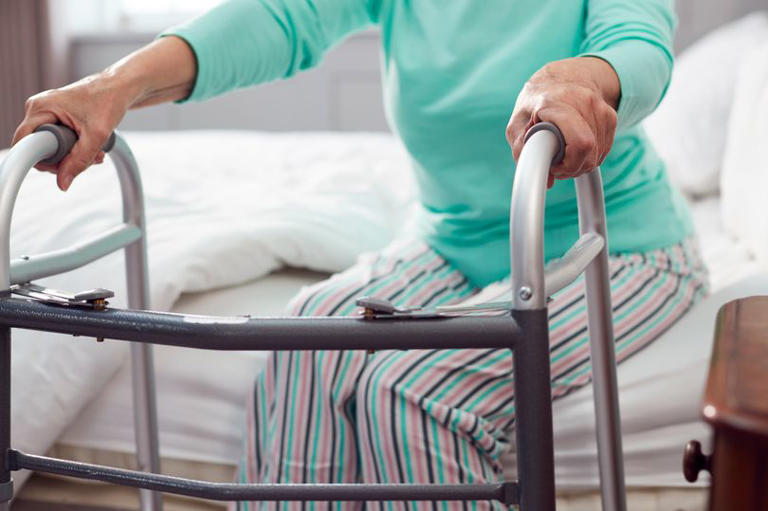 Close Up Of Senior Woman At Home Using Walking Frame To Get Out Of Bed