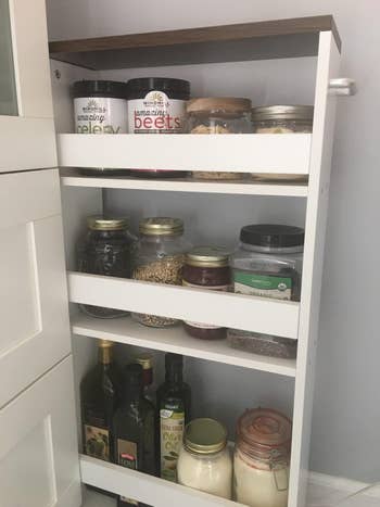 Pull-out pantry filled with various jars, including grains, spices, and oils, organized on three shelves