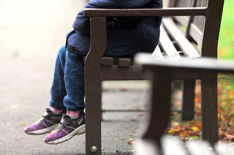 The legs of a child hanging down from a wooden bench on a street