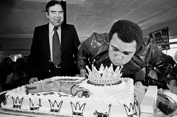 Ali blows out the candles on his birthday cake during a workout at the Fifth Street gym in Miami Beach, Fla., Jan. 17, 1977 while Miami Beach Mayor Leonard Haber looks on.