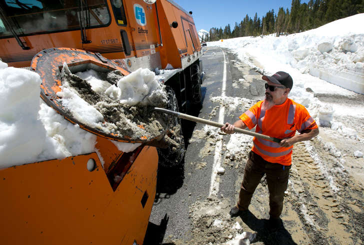 In this photo taken Tuesday, June 6, 2017, Caltrans maintenance worker Paul Jensen removes snow and dirt that is clogging the rotary blower he is operating to clear snow from Highway 120 near near Yosemite National Park, Calif.