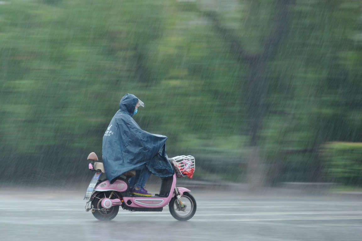 Slide 1 of 40: A woman rides an electric scooter in heavy rain in Fuyang, Anhui province, China June 10, 2017.