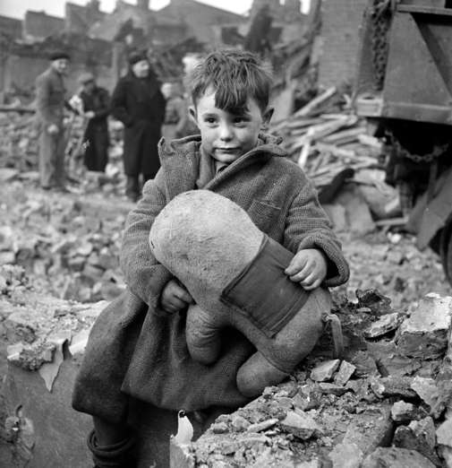Slide 15 de 100: Abandoned boy holding a stuffed toy animal amid ruins following German aerial bombing of London during the Blitz of World War two.