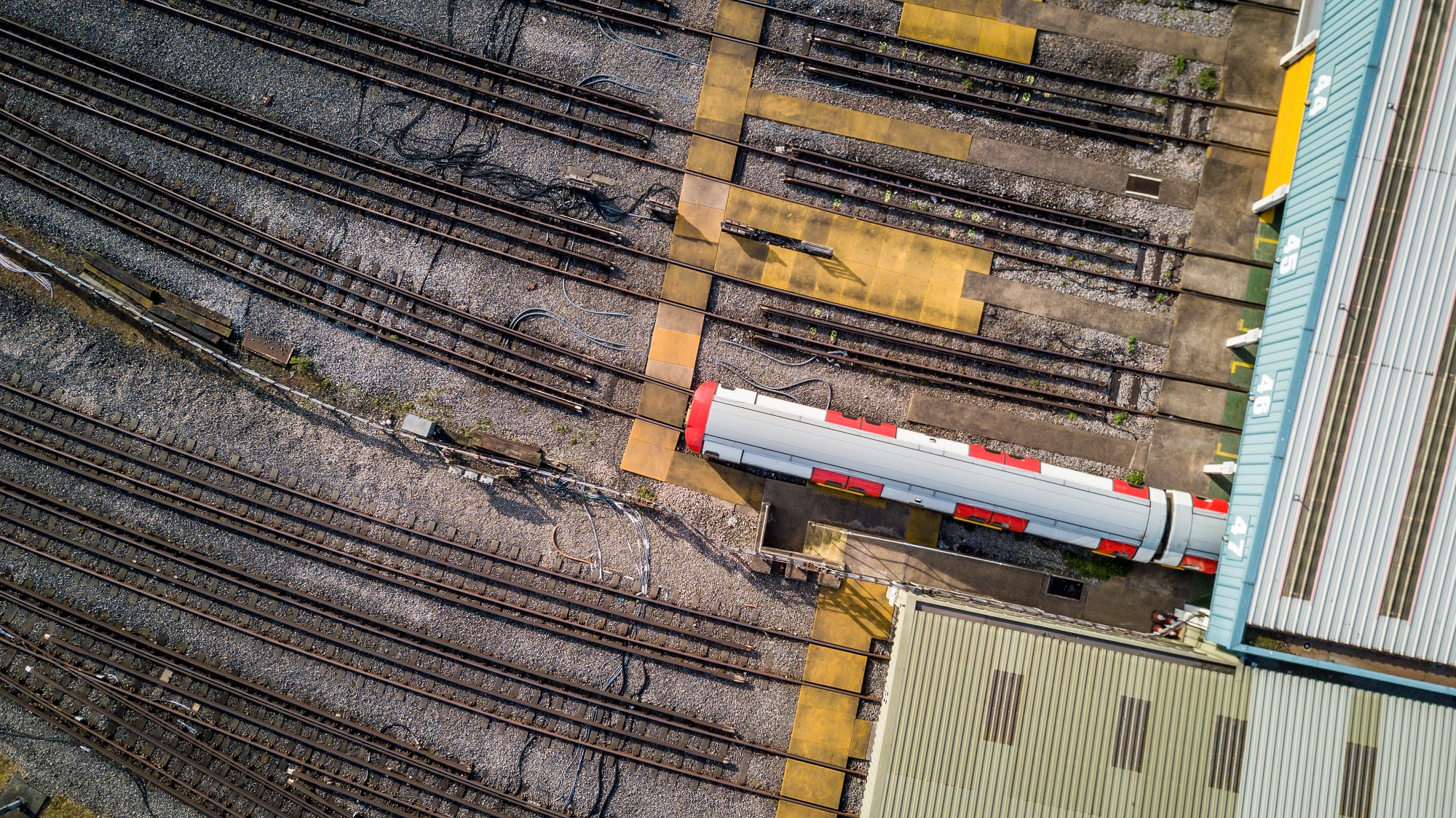 Slide 77 of 100: London Underground tube train depot. Aerial drone photo looking down onto a London tube train emerging from a garage at a North London tube train depot.