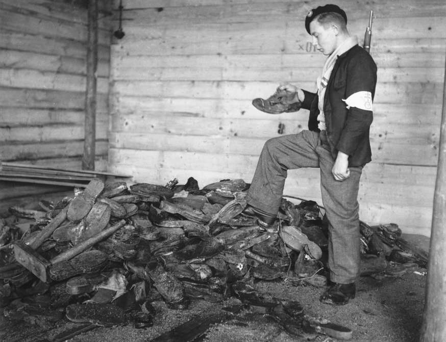 Slide 88 de 100: A French soldier investigates the pile of footwear belonging to victims near the crematorium at Struthof Concentration Camp. | Location: Struthof Camp, near Strasbourg, Alsace, France.