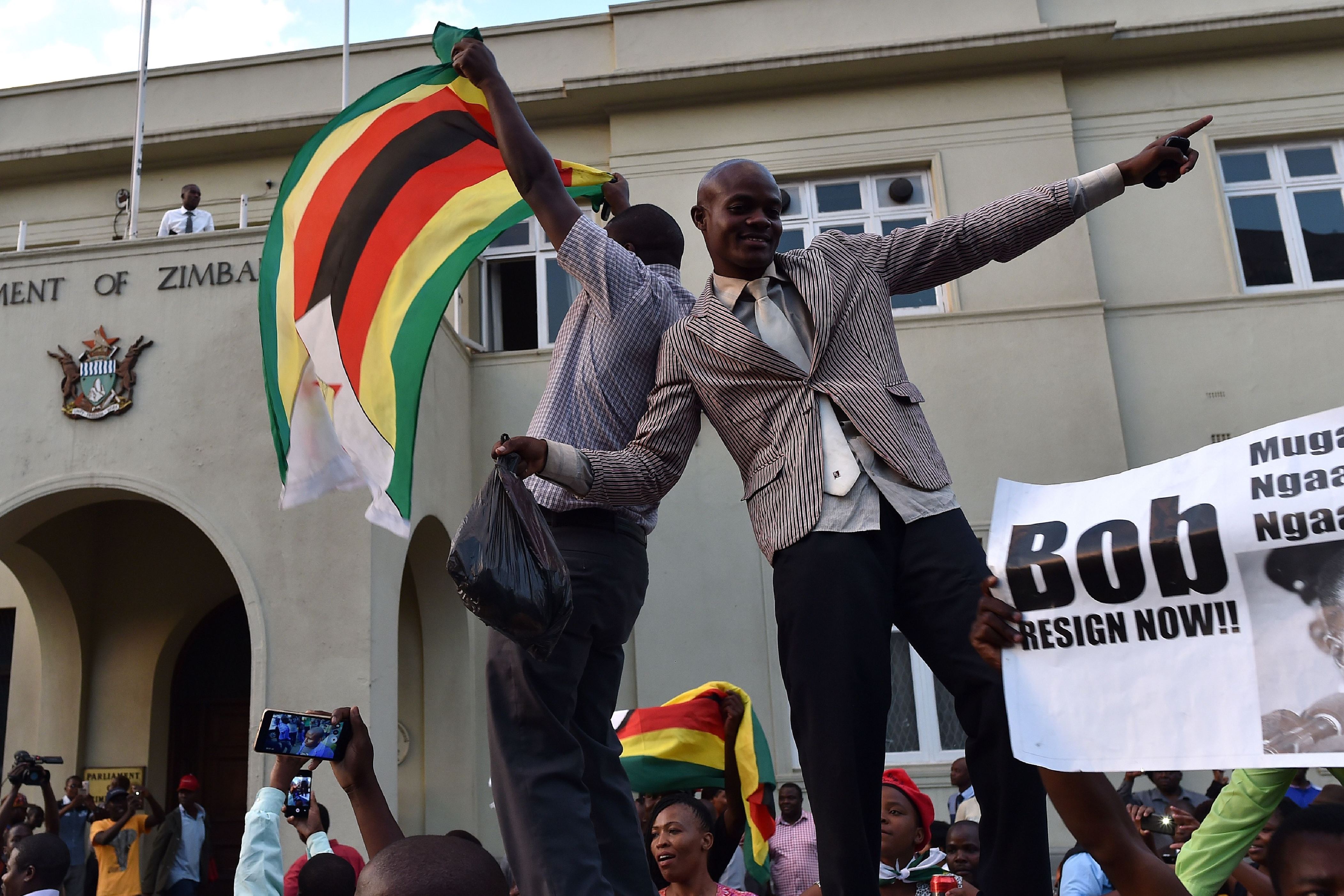 Διαφάνεια 35 από 36: People wave national flags as they celebrate outside the parliament in Harare, after the resignation of Zimbabwe's president Robert Mugabe on November 21, 2017. The bombshell announcement sparks scenes of wild celebration in the streets of Harare, with car horns honking and crowds dancing and cheering over the departure of the autocrat who has ruled Zimbabwe since independence.