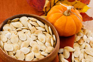 Close up image of toasted pumpkin seeds displayed against a rich background of autumn colors. Horizontal composition has small area in upper left for copy.