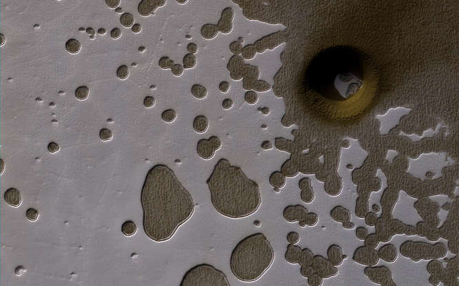 Slide 18 of 86: A late summer view of the Southern hemisphere of Mars seen in this image from NASA's Mars Reconnaissance Orbiter released on June 2. Shallow pits are seen in the bright residual cap of carbon dioxide ice. There is also a deeper, circular formation that penetrates through the ice and dust, possibly an impact crater or a collapse pit.