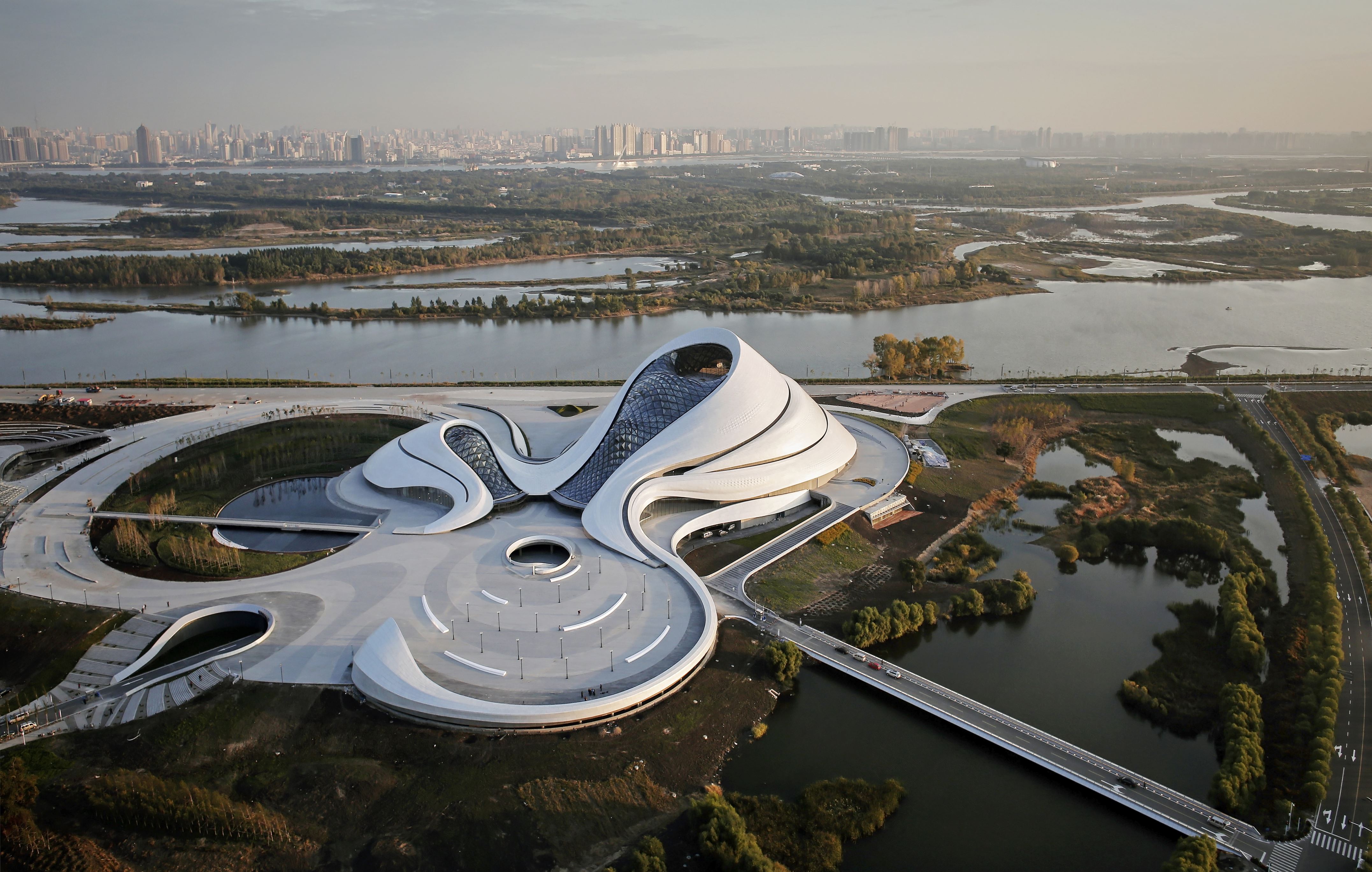 Slide 56 of 57: Aerial View Of Opera House Embedded In Harbin's Wetland Landscape With City Skyline In Background. Harbin Opera House, Harbin, China. Architect: Mad Architects, 2015.