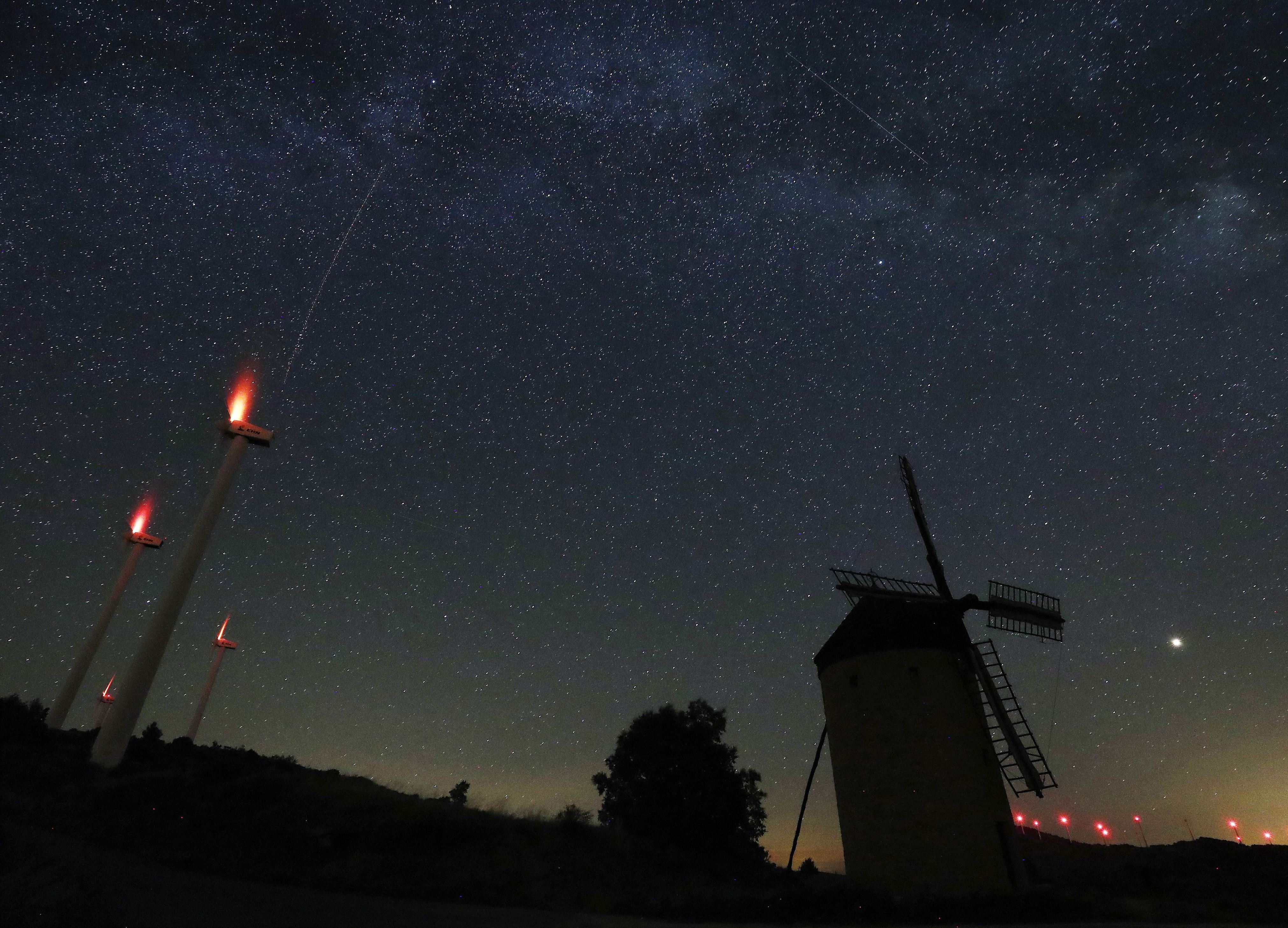 Slide 28 de 33: The Milky Way (up in the sky) is seen over an old mill surrounded by modern windmills on early Aug. 6.