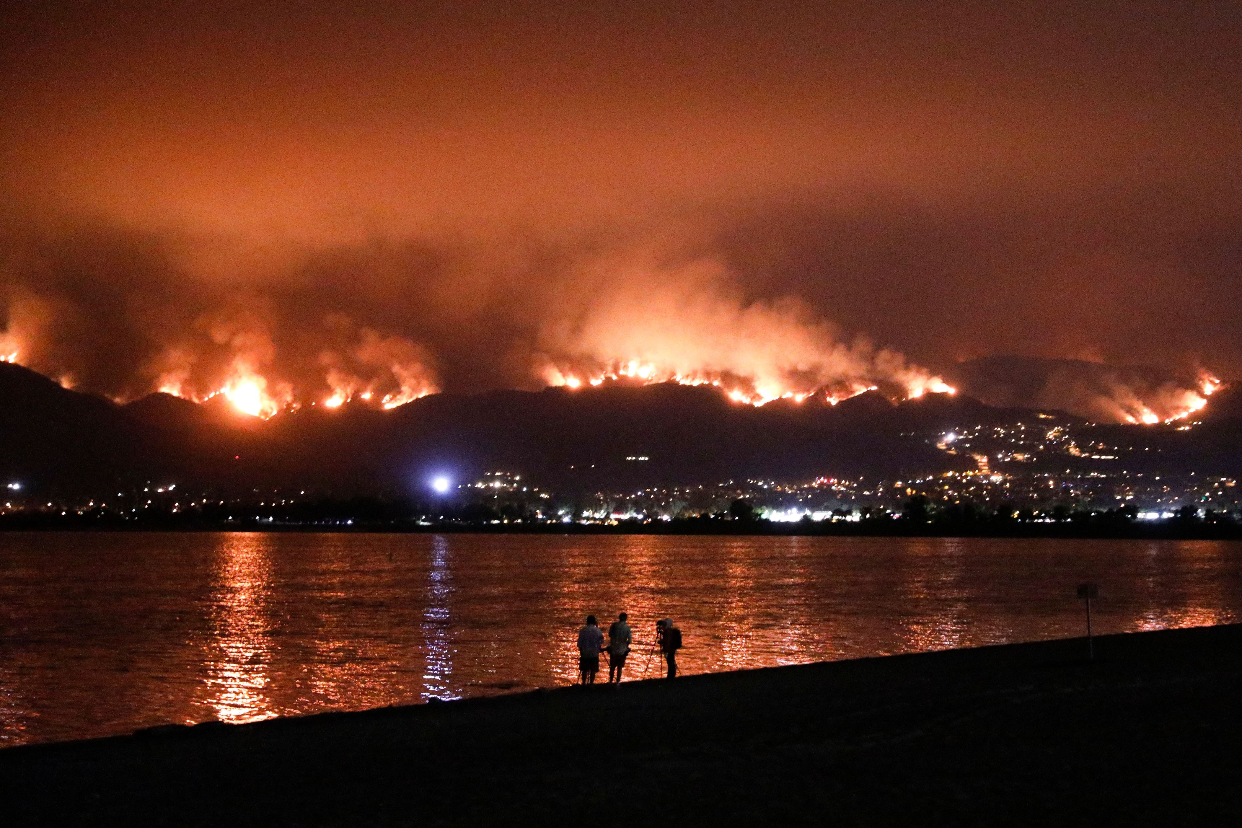 Slide 15 de 33: Onlookers are silhouetted against the reflection of a wildfire burning in the Cleveland National Forest in Lake Elsinore, Calif., . Evacuations have been ordered for several small mountain communities near where a forest fire continues to grow in Southern California