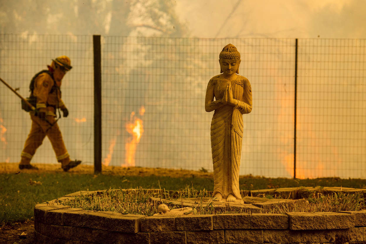Slide 7 of 95: Flames lick behind a Buddha lawn statue as the Ranch Fire tears down New Long Valley Rd near Clearlake Oaks, California, on Saturday, August 4, 2018. - The Ranch Fire is part of the Mendocino Complex, which is made up of two blazes, the River Fire and the Ranch Fire. (Photo by NOAH BERGER / AFP)        (Photo credit should read NOAH BERGER/AFP/Getty Images)