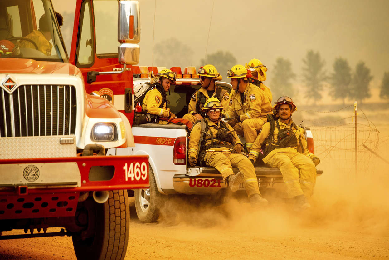 Slide 6 of 95: Firefighters ride in the back of a pickup truck while battling the Ranch Fire on New Long Valley Rd near Clearlake Oaks, California, on Saturday, August 4, 2018. - The Ranch Fire is part of the Mendocino Complex, which is made up of two blazes, the River Fire and the Ranch Fire. (Photo by NOAH BERGER / AFP)        (Photo credit should read NOAH BERGER/AFP/Getty Images)