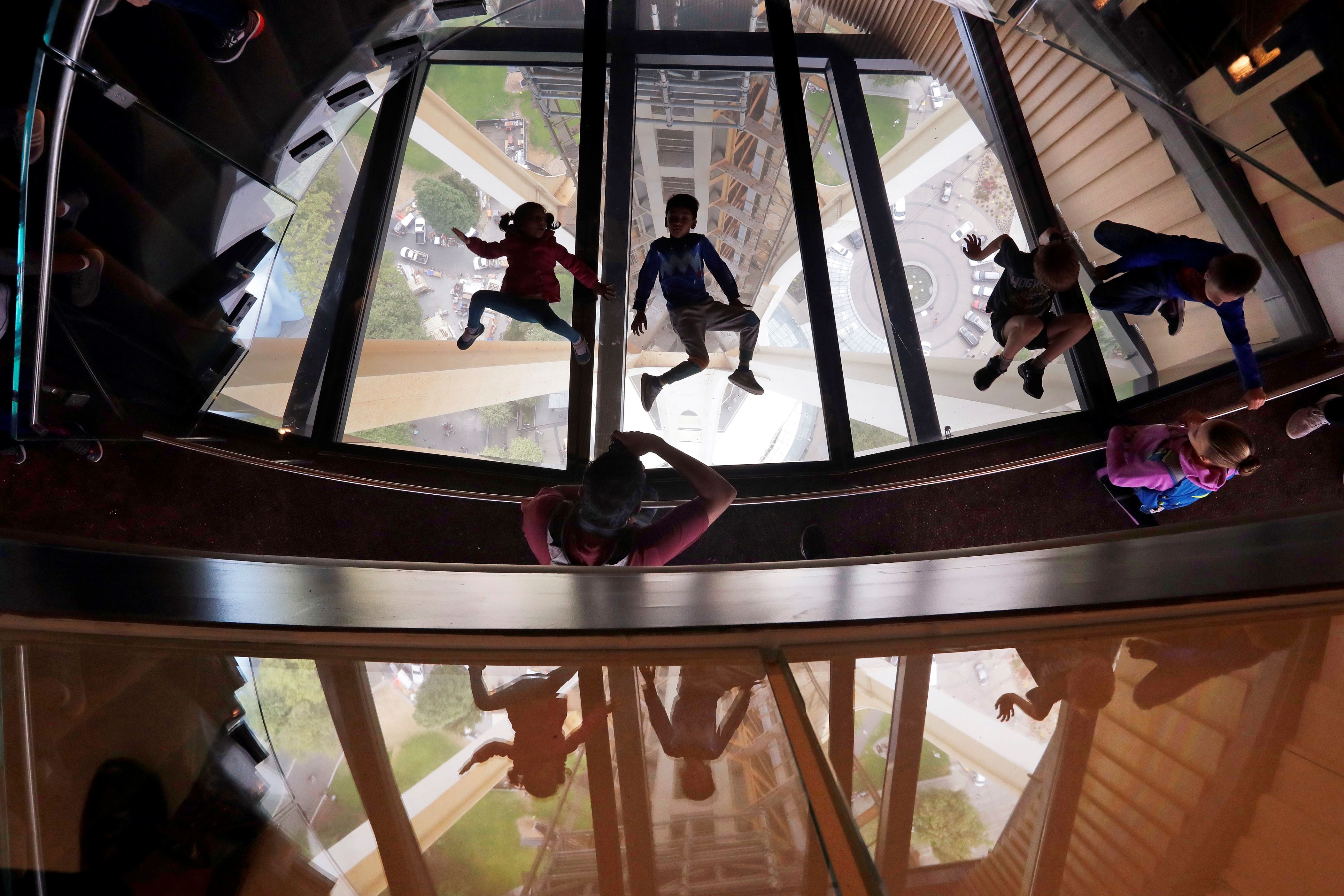 Children lay atop a glass floor, reflected in windows adjacent to it, at the bottom of a new cantilever staircase called the "Oculus Stairs" at the Space Needle Friday, Aug. 3, 2018, in Seattle. The recently completed, $100 million renovation of the 605-foot-tall structure included replacing some floors and walls with structural glass that opened-up views of the three legs below. It also includes "The Loupe," called the world's first and only revolving glass floor. (AP Photo/Elaine Thompson)