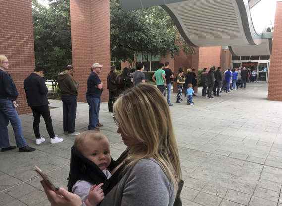 Slide 4 of 15: Megan Heckel of Plano holds her daughter Lily as they wait in line for early voting outside Maribelle M. Davis Library in Plano, Texas, Monday, Oct. 22, 2018. (AP Photo/David Koenig)