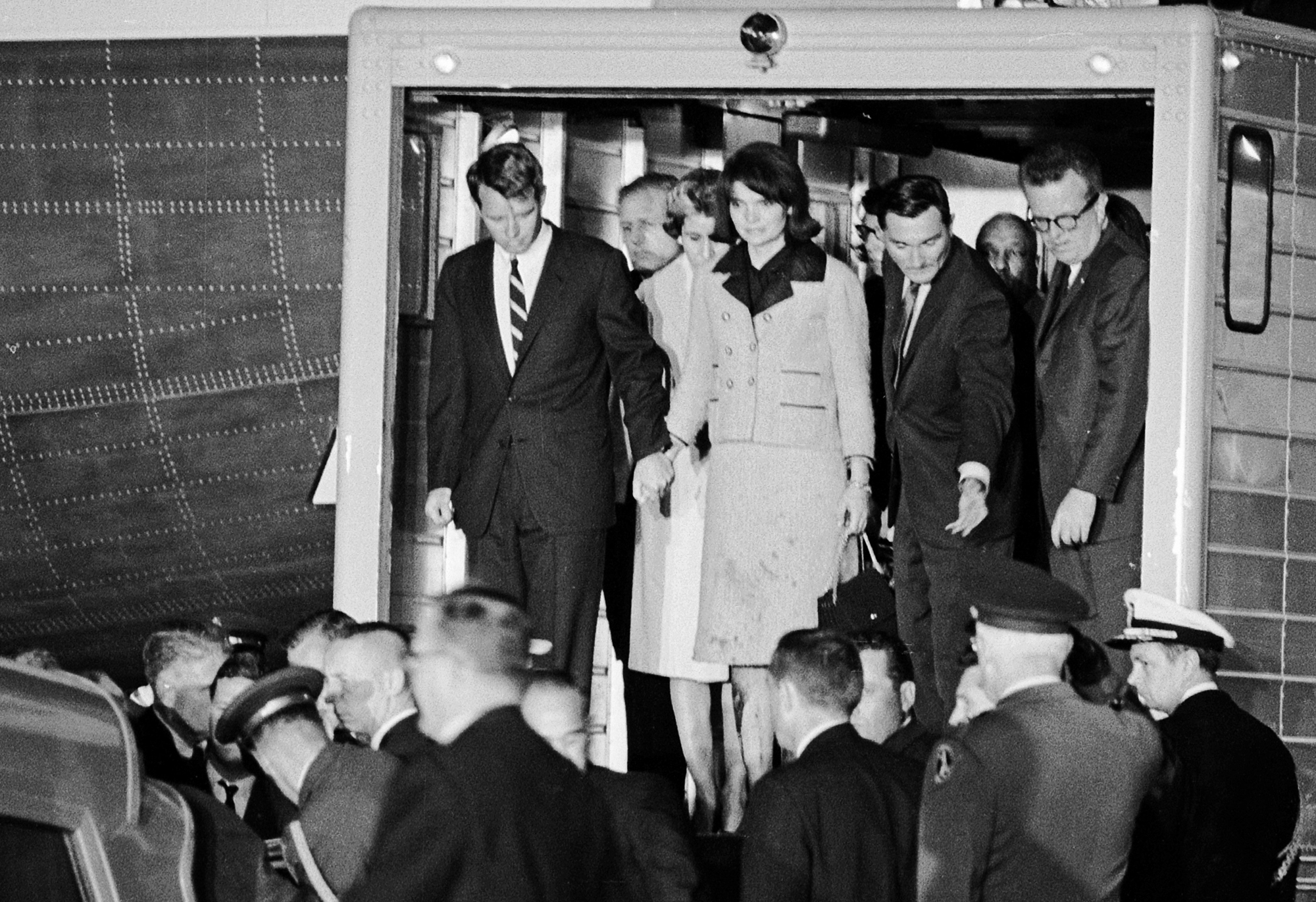 The coffin of President John Fitzgerald Kennedy is moved from Air Force One to an ambulance upon arrival at Andrews Air Force Base. Robert Kennedy, Jacqueline Kennedy, Kenny O'Donnell, and Larry O'Brien stand side-by-side in the doorway. Photo by Wally McNamee/ The Washington Post via Getty Images