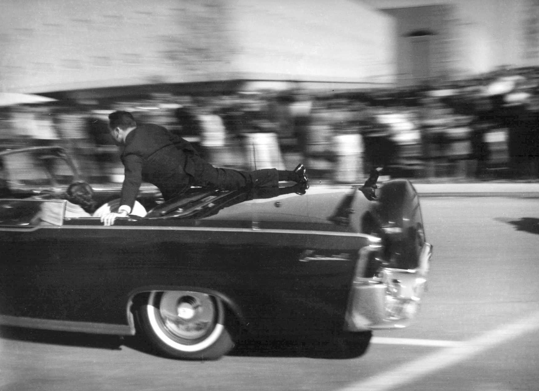 FILE - In this Nov. 22, 1963 file photo, the limousine carrying mortally wounded President John F. Kennedy races toward the hospital seconds after he was shot in Dallas. Secret Service agent Clinton Hill is riding on the back of the car,  (AP Photo/Justin Newman, File)