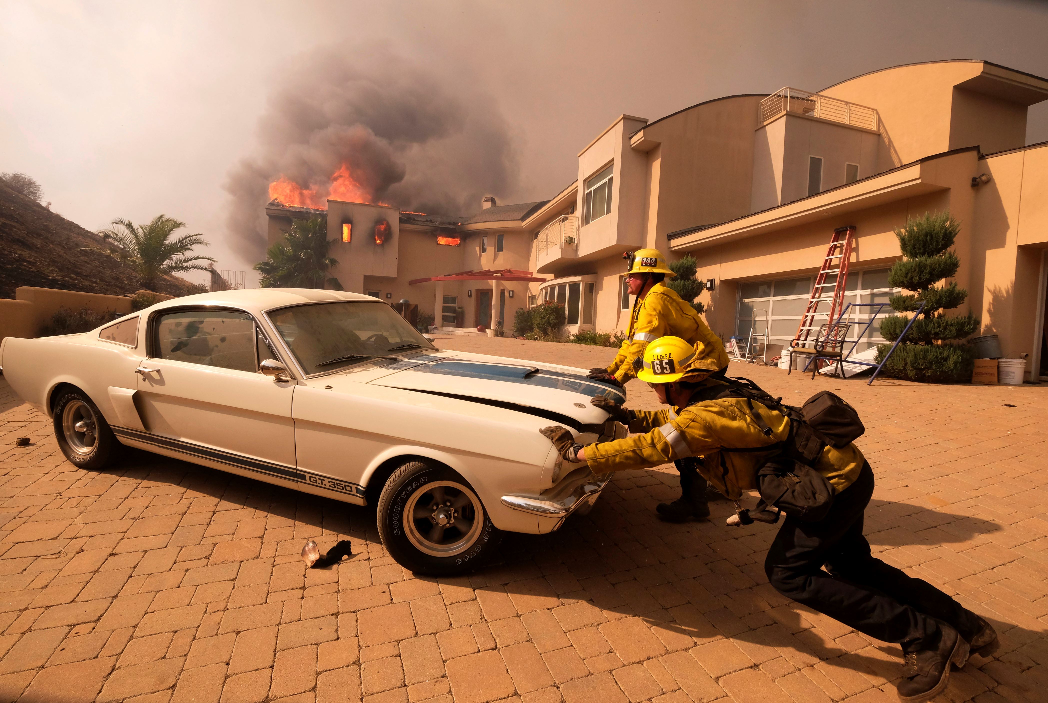 Slide 50 of 57: Firefighters push a vehicle from a garage as a wildfire fire burns a home near Malibu Lake in Malibu, Calif., Friday, Nov. 9, 2018. (AP Photo/Ringo H.W. Chiu)