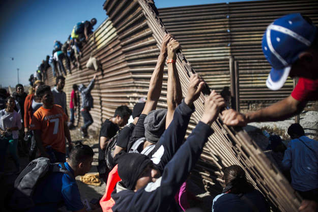 Slide 3 of 50: A group of Central American migrants -mostly Hondurans- climb the border fence between Mexico and the United States as others try to bring it down, near El Chaparral border crossing, in Tijuana, Baja California State, Mexico, on November 25, 2018.