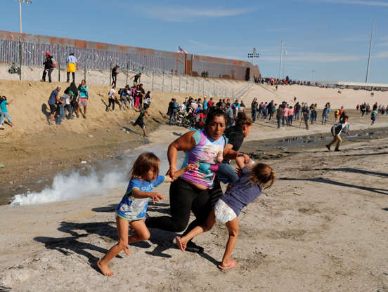 第1页，共50页：一个移民家庭，是前往美国途中从中美洲出发的数千人的大篷车的一部分，于2018年11月25日在墨西哥蒂华纳的美国和墨西哥之间的边界墙前逃离催泪瓦斯。