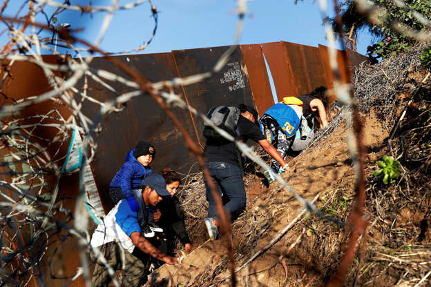 Slide 4 of 50: Migrants, part of a caravan of thousands from Central America trying to reach the United States, climb up a steep hill to find a place to climb over the border wall into the U.S. from Tijuana, Mexico, December 13, 2018. REUTERS/Leah Millis