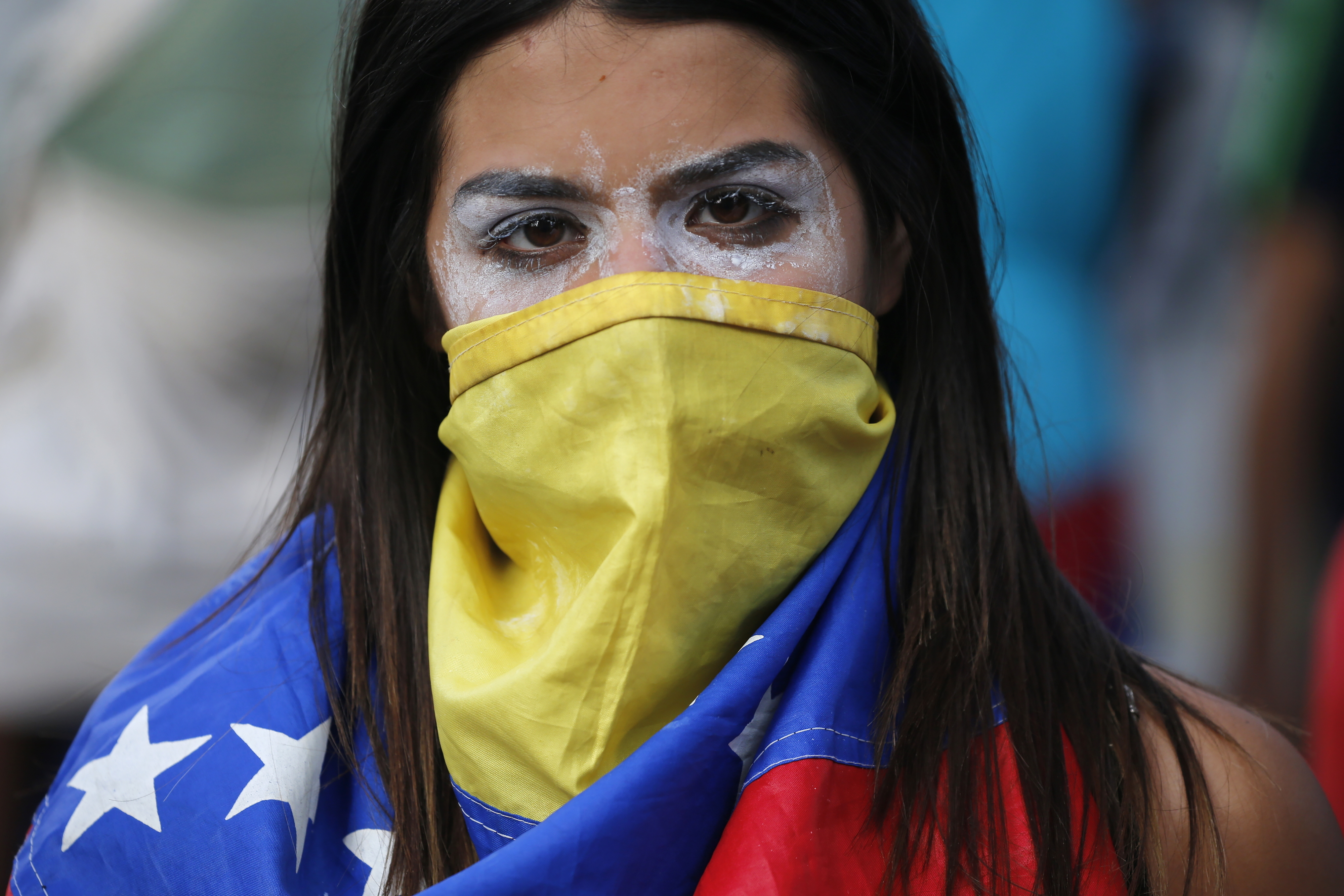 Slide 1 of 64: An anti-government protester covers her face with a Venezuelan flag, and uses toothpaste around her eyes to help lessen the effect of tear gas, during clashes with security forces after a rally demanding the resignation of President Nicolas Maduro in Caracas, Venezuela, Wednesday, Jan. 23, 2019. The head of Venezuela's opposition-run congress declared himself interim president at the rally, until new elections can be called.