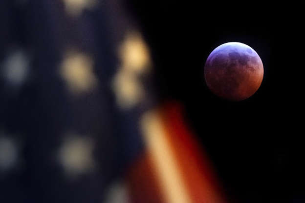 Slide 4 of 29: A U.S. Flag in downtown Washington flies in front of the moon during a lunar eclipse, Sunday, Jan. 20, 2019. The entire eclipse will exceed three hours. Totality - when the moon