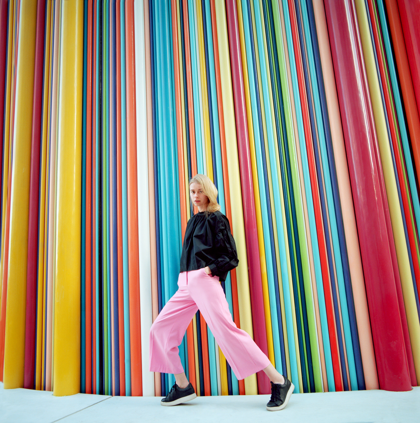 Portrait of young beautiful woman with long blond hair wearing black blouse and pink pants on colorful background. Shot on medium format film camera