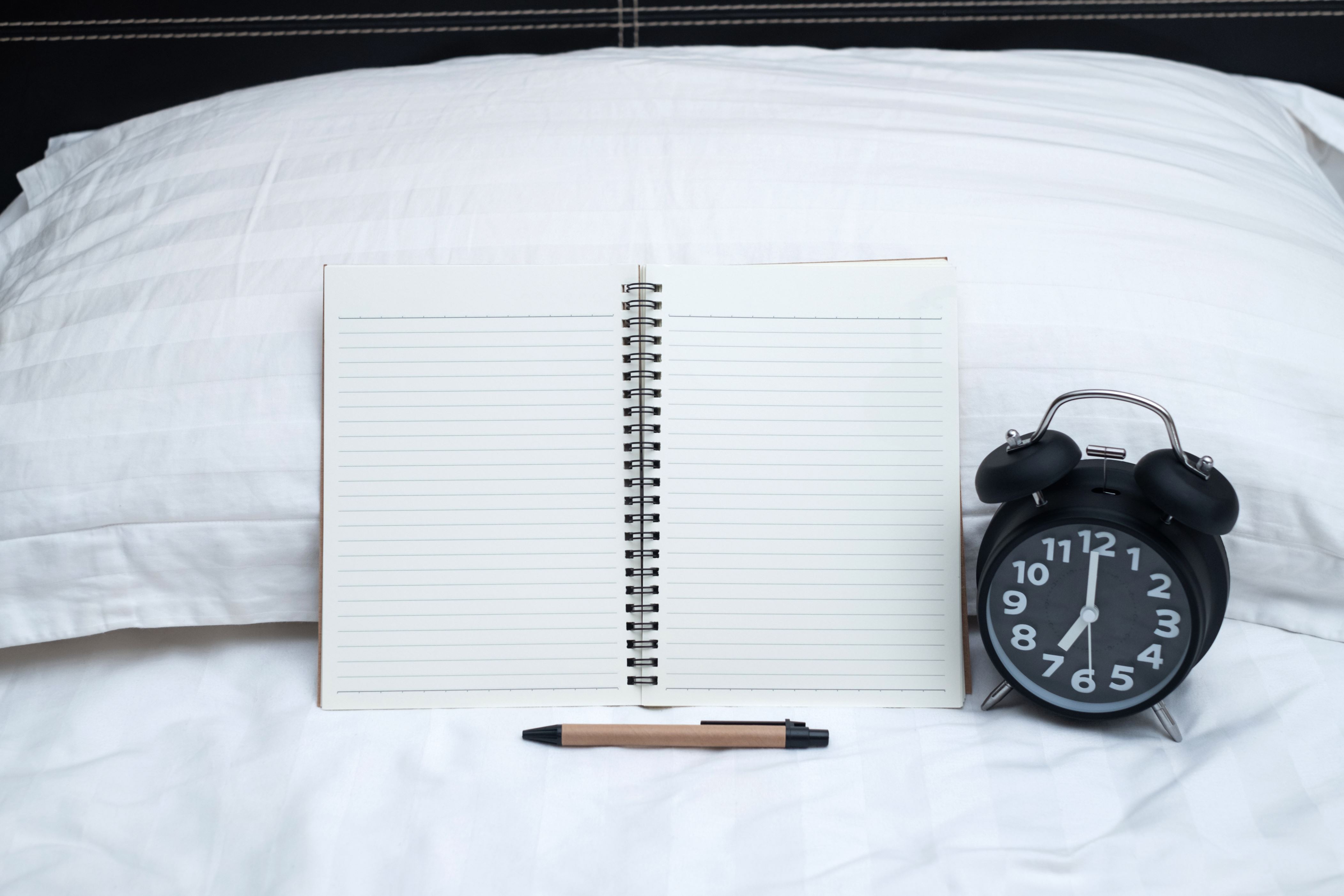 Diary or notebook and vintage alarm clock on bed in bedroom at home or hotel, working or note something before sleep.