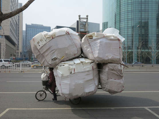 Slide 44 de 45: A woman rides a tricycle overloaded with recyclable rubbish