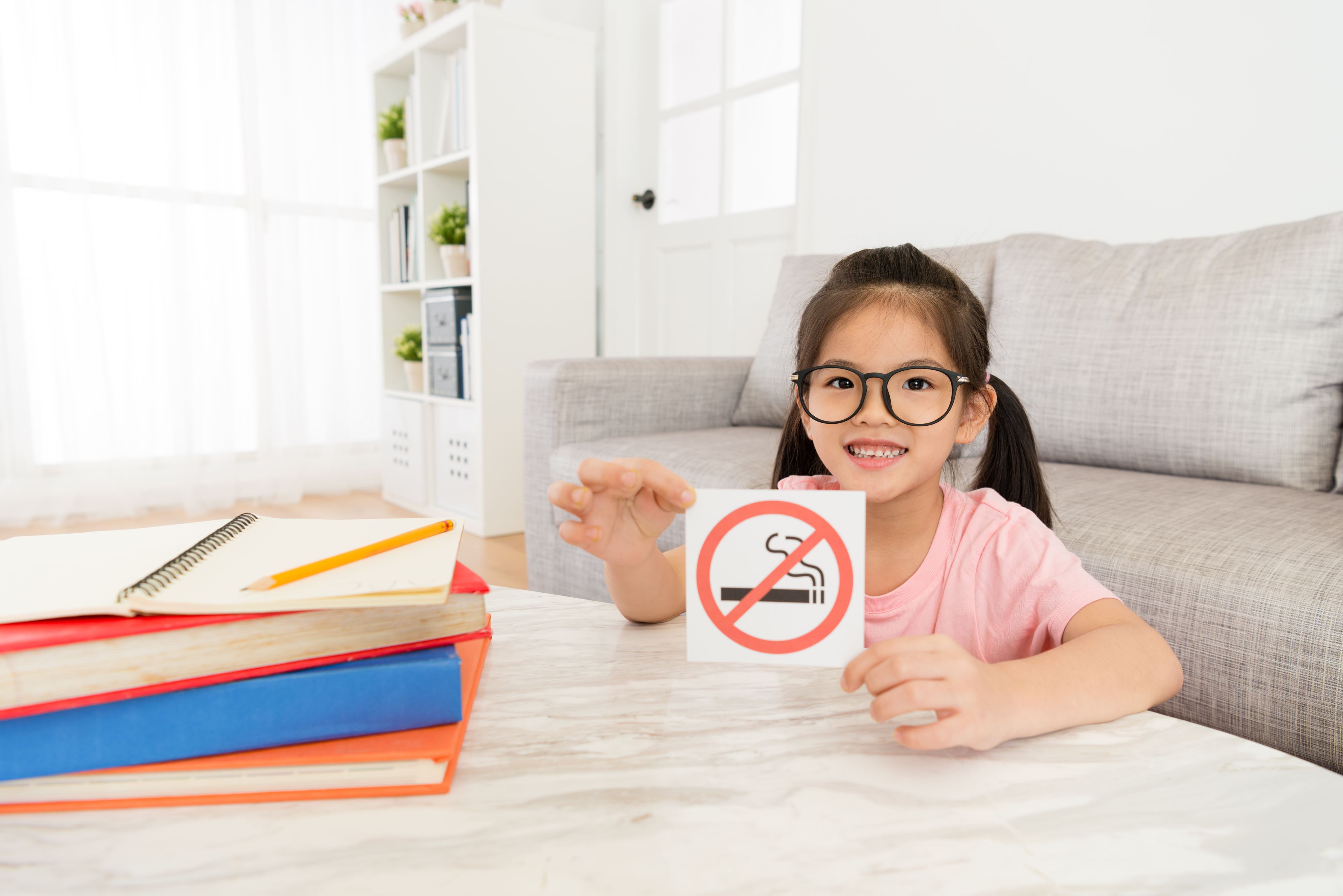 smiling lovely little girl looking at camera presenting no smoking notice.