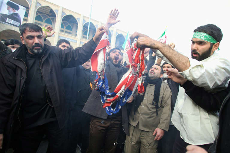 a man standing in front of a crowd posing for the camera: Iranians burn a US flag during a demonstration against American "crimes" in Tehran  following the killing of Iranian Revolutionary Guards Major General Qasem Soleimani in a US strike on his convoy at Baghdad international airport