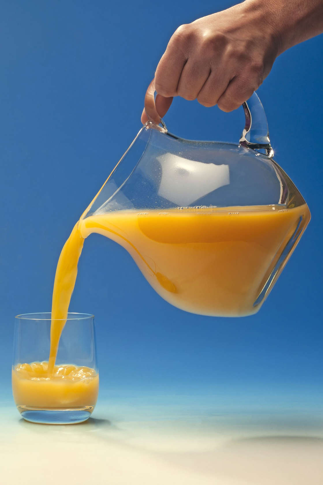 Hand pouring orange juice out of a jug into a glass
