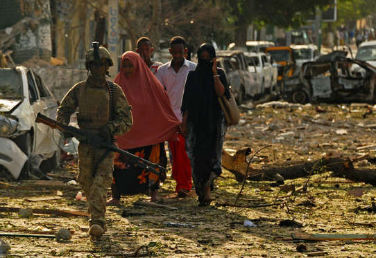 Women walk next to a military on the scene of a terror attack on the Ambassador Hotel claimed by Somalia's Al-Qaeda-linked Shabaab, in Mogadishu on June 2, 2016. At least 10 people, including two lawmakers, were killed in a car bomb and gun attack on 